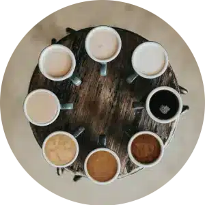 Circular image of a variety of different coffees on a round wooden table.