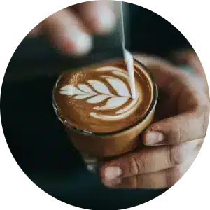 Circular image of a person making a latte with latte art.